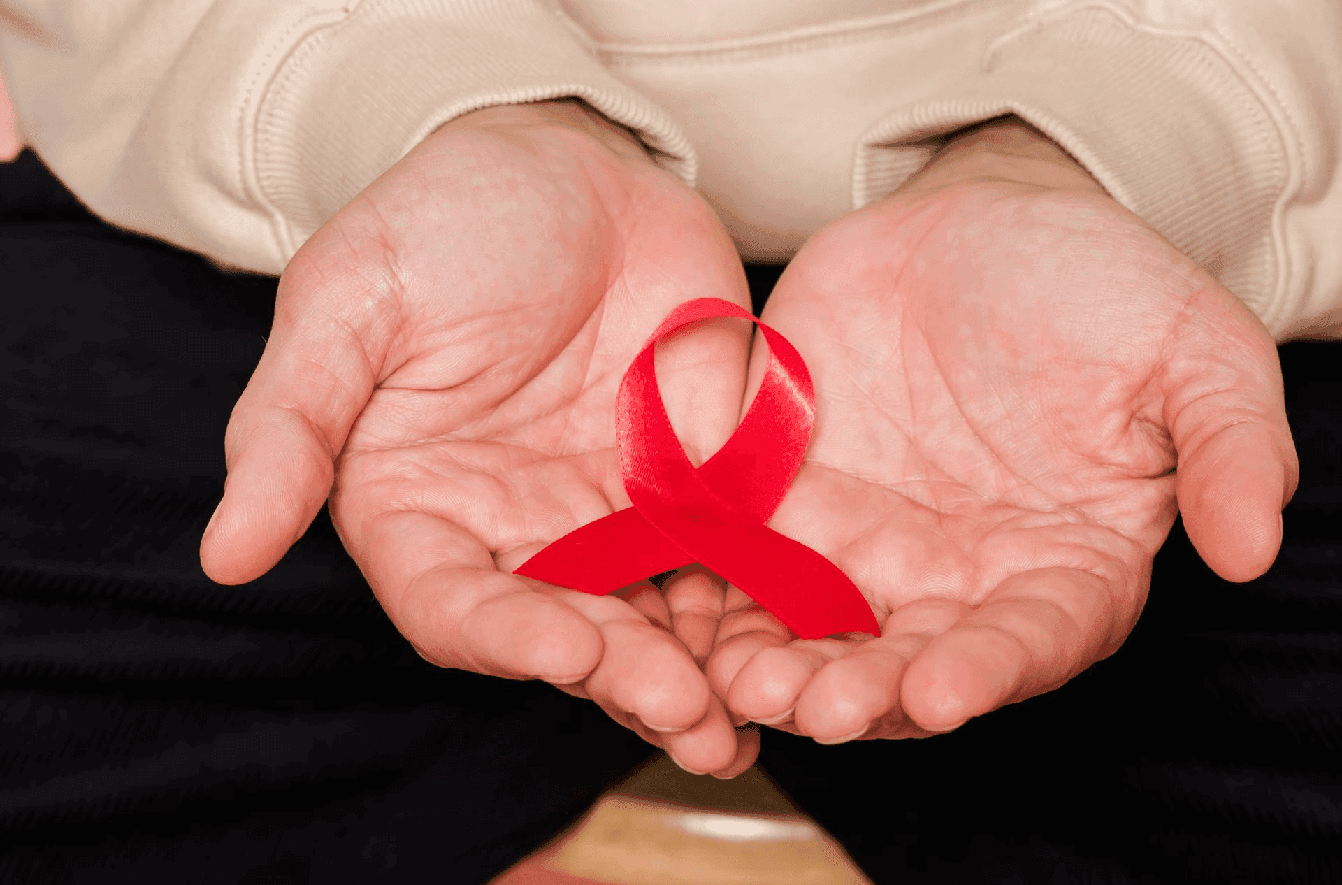 Twee handen met een rood aidslintje erin