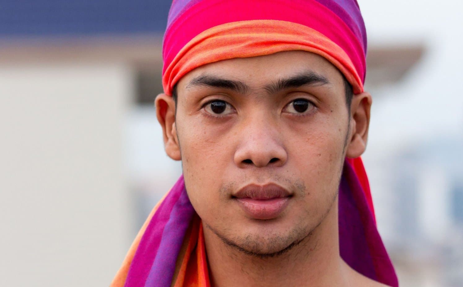 Man met een geweven regenboogsjaal als hoofddoek om